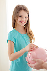 Image showing smiling little girl putting coin into piggy bank