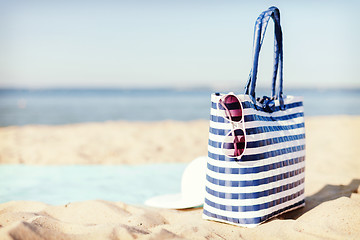 Image showing straw hat, sunglasses and bag lying in the sand