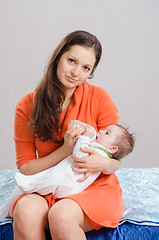 Image showing Mum feeds from a bottle six-month daughter sitting on bed