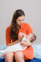 Image showing Mum feeds from bottle daughter sitting on a bed