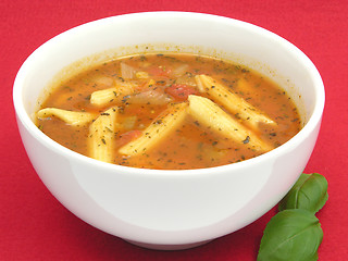 Image showing Noodle soup with tomatoes and herbs on red