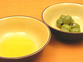 Image showing Two bowls of ceramic with olive oil and olives on orange background