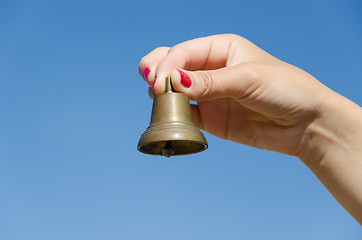 Image showing Woman hand red nails hold iron bell on blue sky 