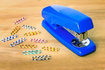 Image showing Stapler of bright blue color and paper clip against a table.