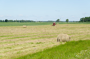 Image showing Dry haystack roll and blur tractor ted hay field 