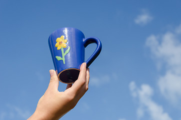 Image showing blue clay cup flower in hand blue sky background 