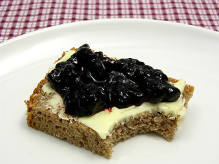 Image showing Bitten into a wholemeal butterbread  with bilberry jam placed on a round plate arranged on a placemat