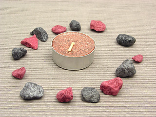 Image showing Tea candle surrounded by decoration stones on a brown background