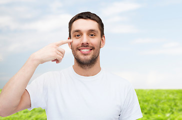 Image showing smiling young handsome man pointing to eyes