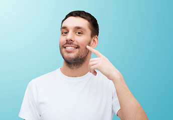 Image showing smiling young handsome man pointing to cheek