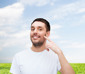 Image showing smiling young handsome man pointing to cheek