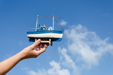 Image showing female hand hold wooden ship toy on sky background 