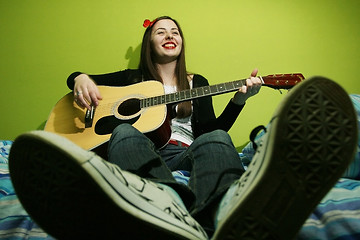 Image showing Young brunette playing guitar on bed