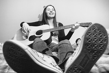 Image showing Young brunette playing guitar on bed black and white