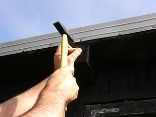 Image showing Man bangs a nail into a wooden wall