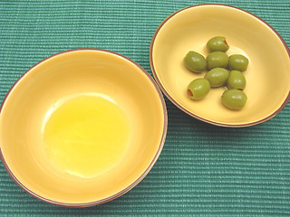 Image showing Two bowls of ceramic with olive oil and olives on green background