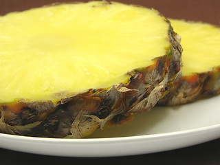 Image showing Two slices of pineapple on a white plate and brown placemat