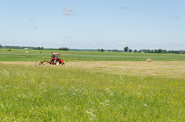 Image showing Red tractor ted hay dry grass in agriculture field 