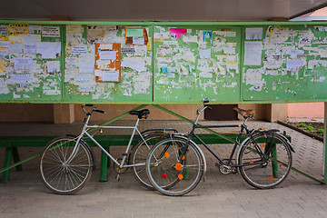 Image showing Two Old Bicycle Leaning Against A Bulletin Board On The Street