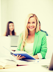 Image showing smiling young woman reading book at school