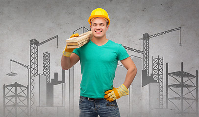 Image showing smiling manual worker in helmet with wooden boards