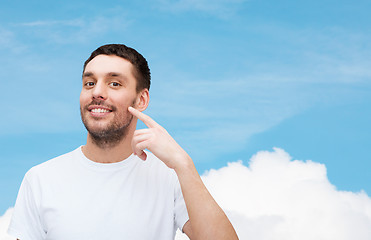 Image showing smiling young handsome man pointing to cheek