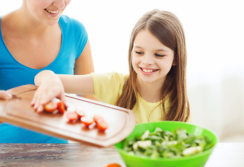 Image showing little girl with mother adding tomatoes to salad