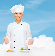 Image showing smiling female chef with salad and cake on plates