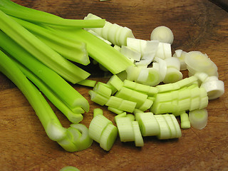 Image showing Sliced spring onions on brown wooden plate