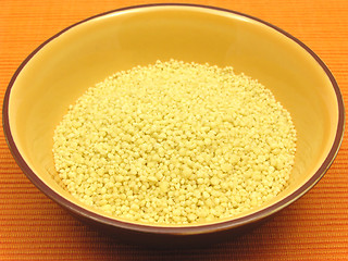 Image showing Yellow couscous in a orange bowl of ceramic on an orange background