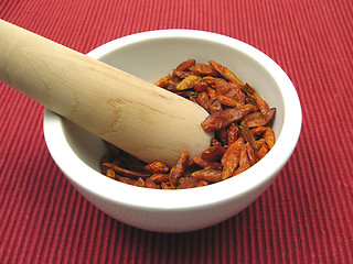 Image showing Pestling dried red hot chili pepper in a bowl of chinaware