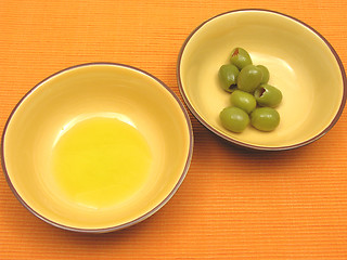 Image showing Two bowls of ceramic with olive oil and olives on orange background