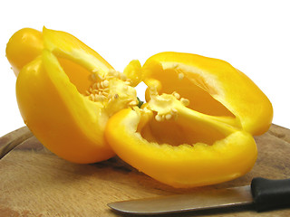 Image showing Halved yellow pepper on wooden plate  with knife