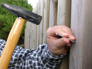 Image showing Man bangs a nail into a wooden wall