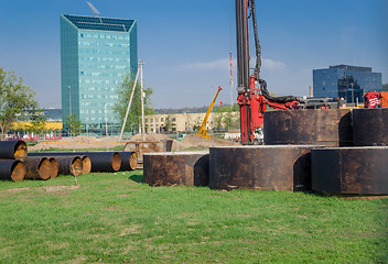 Image showing worksite equipment pipes near glass skyscraper 