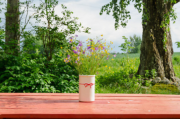 Image showing vase with wild flowers standing outside red table 