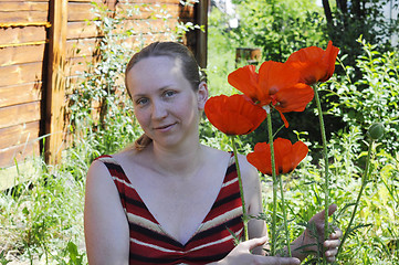 Image showing The woman with red poppies in a garden.