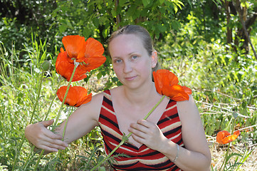 Image showing The woman with red poppies in a garden.