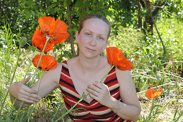 Image showing The woman with red poppies in a garden.