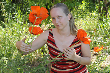 Image showing The woman with red poppies in a garden.