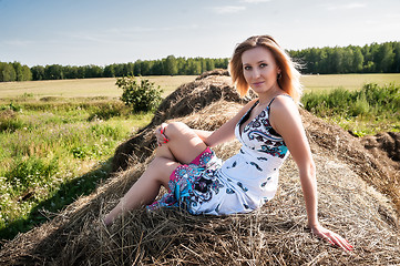 Image showing Young blond woman sits on hay