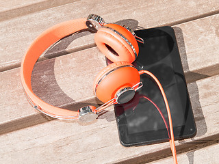 Image showing Vibrant orange headphones and black tablet pc on wooden bench