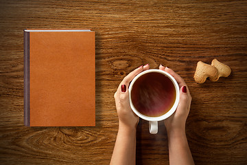 Image showing woman with cup of tea, cookies and book on wood