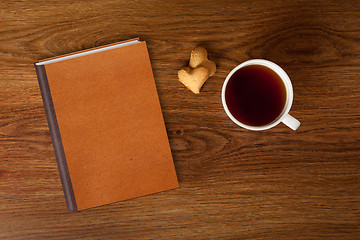Image showing woman with cup of tea, cookies and book on wood
