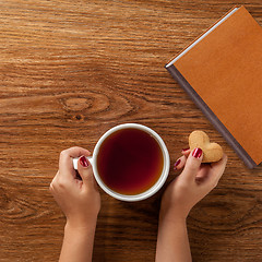 Image showing woman holding hot cup of tea with cookies