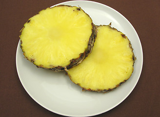 Image showing Two slices of pineapple on a white plate and brown placemat