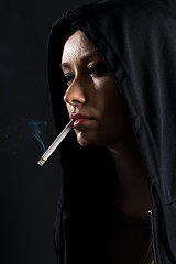Image showing Young woman on a black background smoking a cigarette