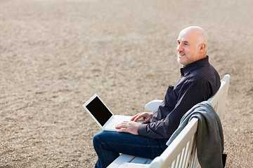 Image showing Man sitting on a bench using a laptop