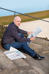 Image showing Man sitting on steps reading a newspaper