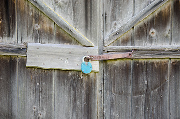 Image showing wooden barn door with iron  blue lock hanging 